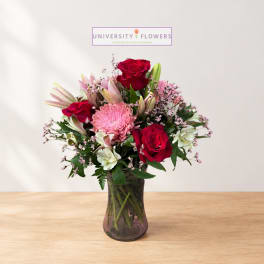 Bouquet of red roses, pink blooms, and lilies in a glass vase