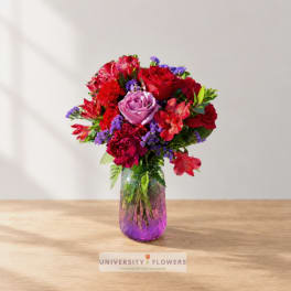 Mixed bouquet of red, pink, and purple flowers in a glass vase