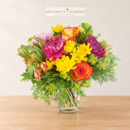 Mixed bouquet in a clear glass vase with yellow, pink, purple, and orange blooms