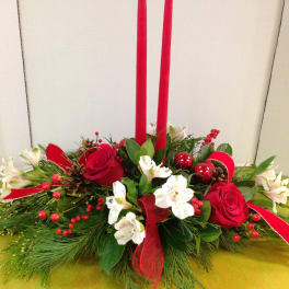 Red roses and white flowers in a low holiday centerpiece with tall red candles