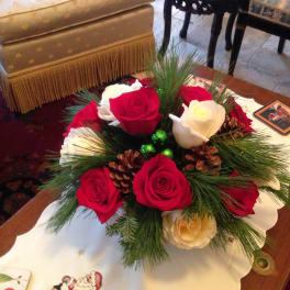 Red and white roses arranged with pine and pinecones in a low centerpiece
