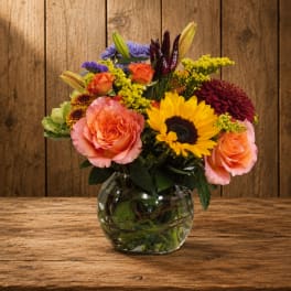 Mixed bouquet of roses, sunflowers, lilies, and chrysanthemums in a glass vase