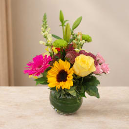 Mixed bouquet in a round glass vase with a yellow rose, sunflower, and pink blooms