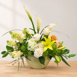 White calla lilies and roses in a low green vase with yellow blooms