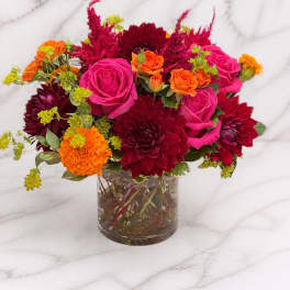Bright mixed bouquet of pink roses, orange blooms, and burgundy flowers in a glass vase