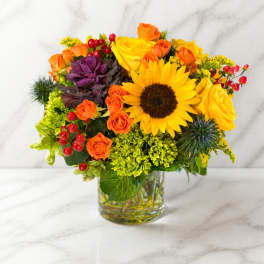 Bright mixed bouquet with sunflowers, orange roses, and red berries in a glass vase