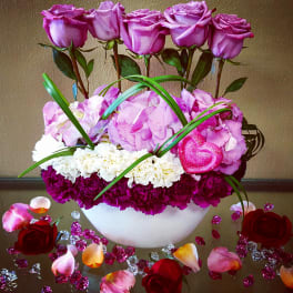 Pink roses and carnations arranged in a white bowl with decorative petals.