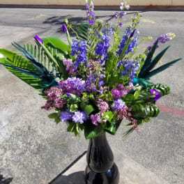 Tall purple and blue floral arrangement in a black vase