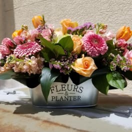 Mixed bouquet of pink, peach, and orange flowers in a metal planter