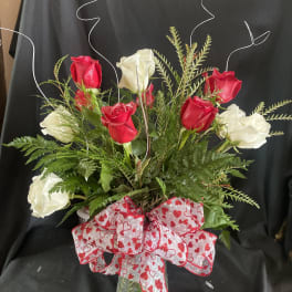 Red and white roses in a glass vase with a heart-patterned bow