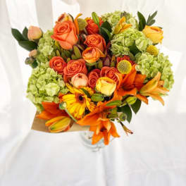 Bouquet of orange roses, lilies, and green hydrangeas in kraft wrap and glass vase