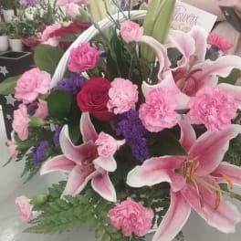 Basket arrangement of pink lilies, pink carnations, purple filler, and a red rose