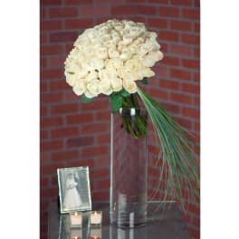 Cream rose bouquet in a tall glass vase with a long grass accent.