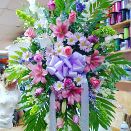Large floral standing spray with pink lilies, roses, and daisies, tied with a lavender bow