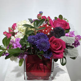 Pink and purple mixed flower arrangement in a red glass vase
