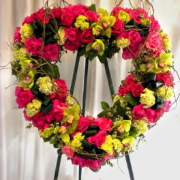 Heart-shaped floral wreath of pink roses and yellow blooms on an easel