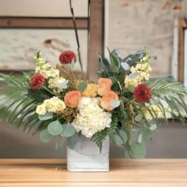Mixed floral arrangement in a white square vase with peach and cream blooms