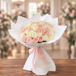 Bouquet of pale pink and cream roses wrapped in white paper with a pink ribbon