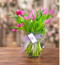 Pink tulips in a clear glass vase with a lavender ribbon