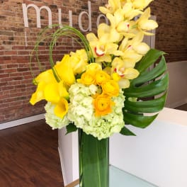 Yellow orchids, calla lilies, and roses arranged in a tall glass vase