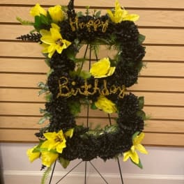 Black and yellow floral standing wreath on an easel with birthday lettering