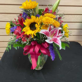 Mixed bouquet with sunflowers, lilies, and a pink ribbon in a glass vase