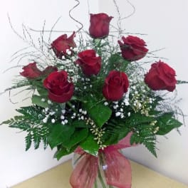 Red roses arranged in a clear glass vase with a pink ribbon