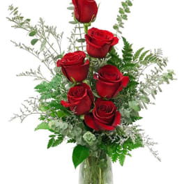 Red roses arranged in a clear glass vase with airy greenery