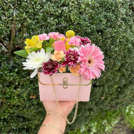 Pink floral arrangement in a small handbag-shaped box with a chain strap