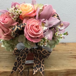 Pink roses and orchids arranged in a small vase with leopard-print ribbon.