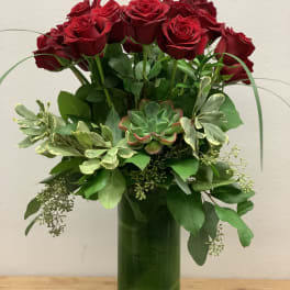 Red roses arranged in a tall green glass vase with mixed greenery.