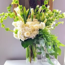 White floral arrangement in a clear glass vase with green accents