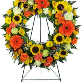 Circular wreath of sunflowers, orange gerberas, and roses on a stand