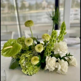 Green and white floral centerpiece with hydrangeas, roses, and tall blooms on a table