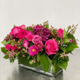 Pink and purple mixed flower arrangement in a clear rectangular vase