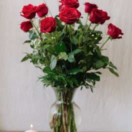 Red roses arranged in a clear glass vase with greenery