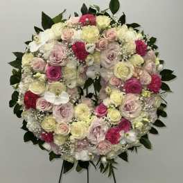 Round floral wreath on an easel with pink, white, and yellow blooms