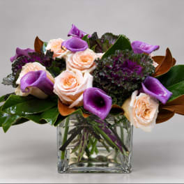 Purple calla lilies and pale peach roses in a clear glass vase