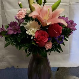 Bouquet of lilies, roses, and purple alstroemeria in a dark vase