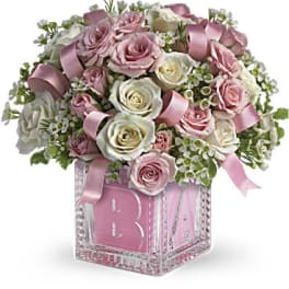 Pink and white roses arranged in a glass cube vase with a pink ribbon