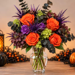 Orange roses and purple flowers in a clear glass vase
