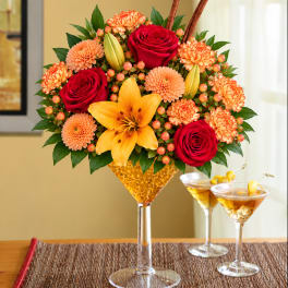 Bouquet of red roses, orange carnations, and a yellow lily in a tall glass vase
