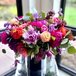 Colorful mixed bouquet in a clear glass vase with purple, pink, and peach blooms