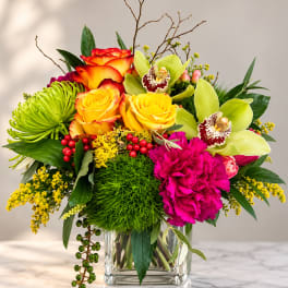 Colorful bouquet in a clear glass vase with roses, orchids, and carnations