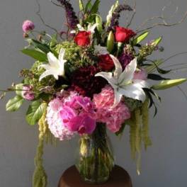 Tall mixed bouquet in a glass vase with red roses, white lilies, and pink blooms
