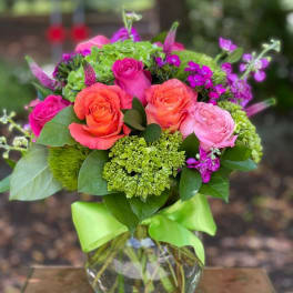 Pink and orange roses in a glass vase with green accents