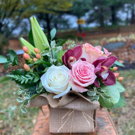 Pink and white roses with purple orchids in a burlap-wrapped box