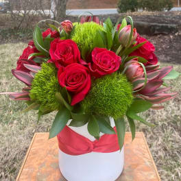 Red roses and green pom-pom flowers in a white hatbox with a red ribbon
