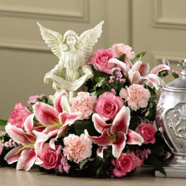 Pink roses and lilies arranged with an angel figurine and silver urn