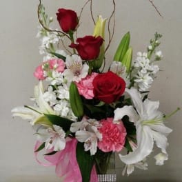 Tall bouquet of red and white flowers in a clear glass vase with pink ribbon